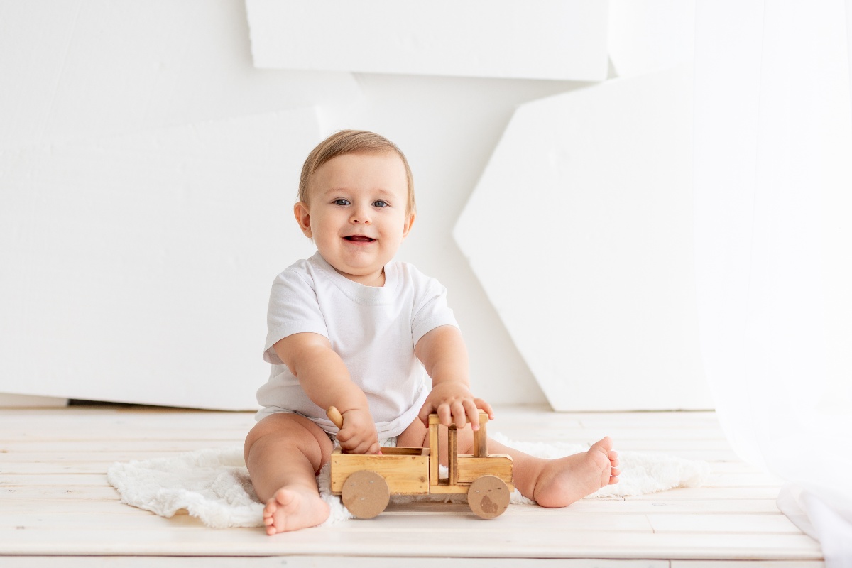 Bambino sorridente seduto a terra mentre gioca con una macchinina di legno.