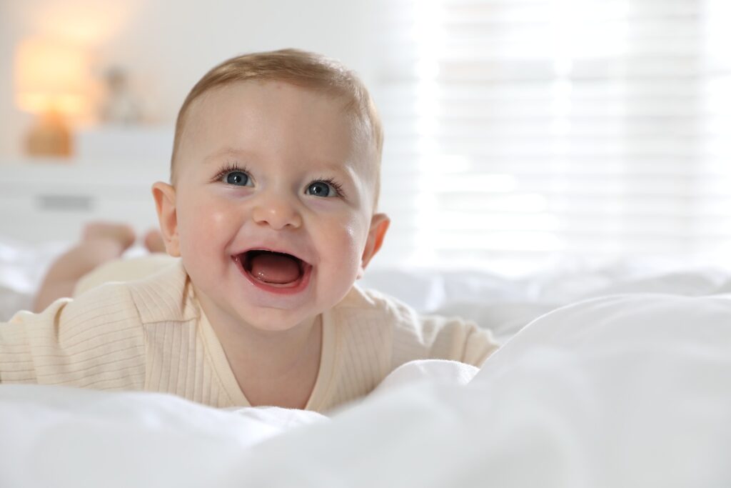Neonato sorridente disteso su un morbido letto bianco.