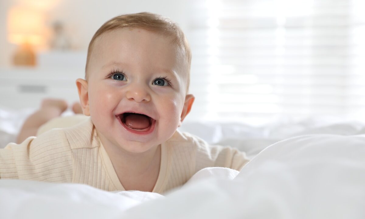 Neonato sorridente disteso su un morbido letto bianco.