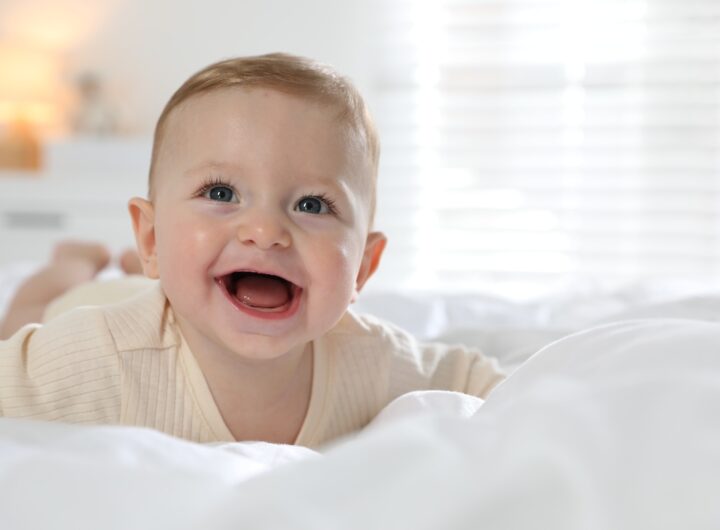 Neonato sorridente disteso su un morbido letto bianco.
