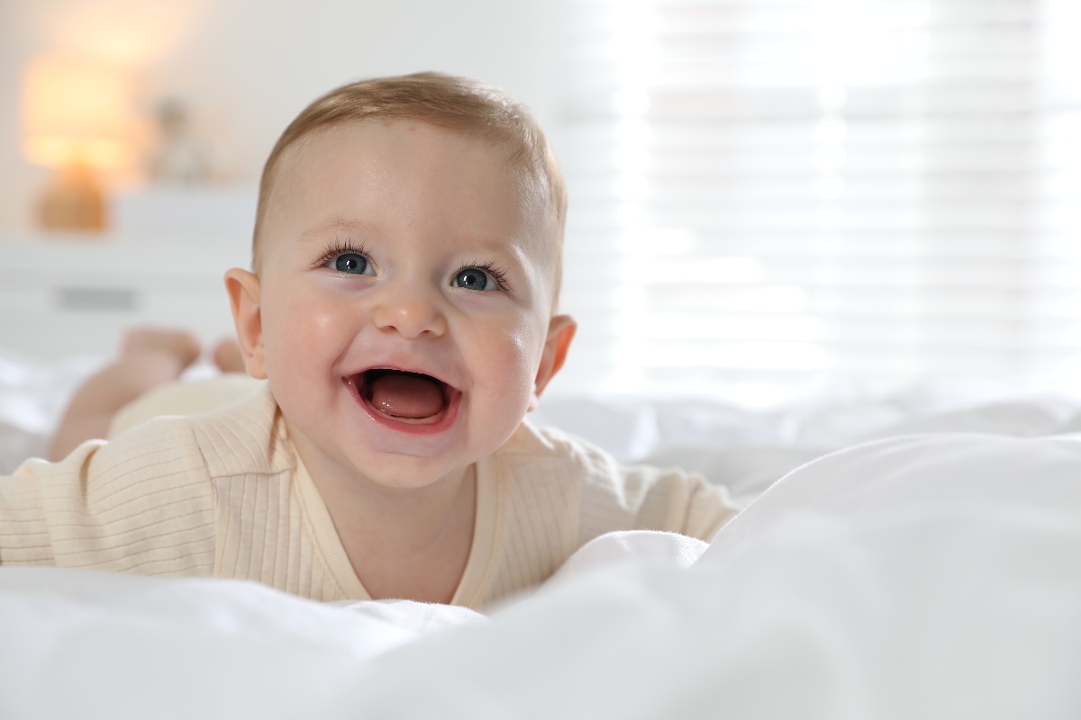 Neonato sorridente disteso su un morbido letto bianco.