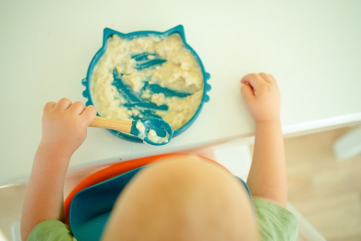 Scena tenera di bimbo che impara a usare il cucchiaino durante lo svezzamento. Bambino nello svezzamento che tenta di mangiare cibi solidi da solo con il cucchiaino.