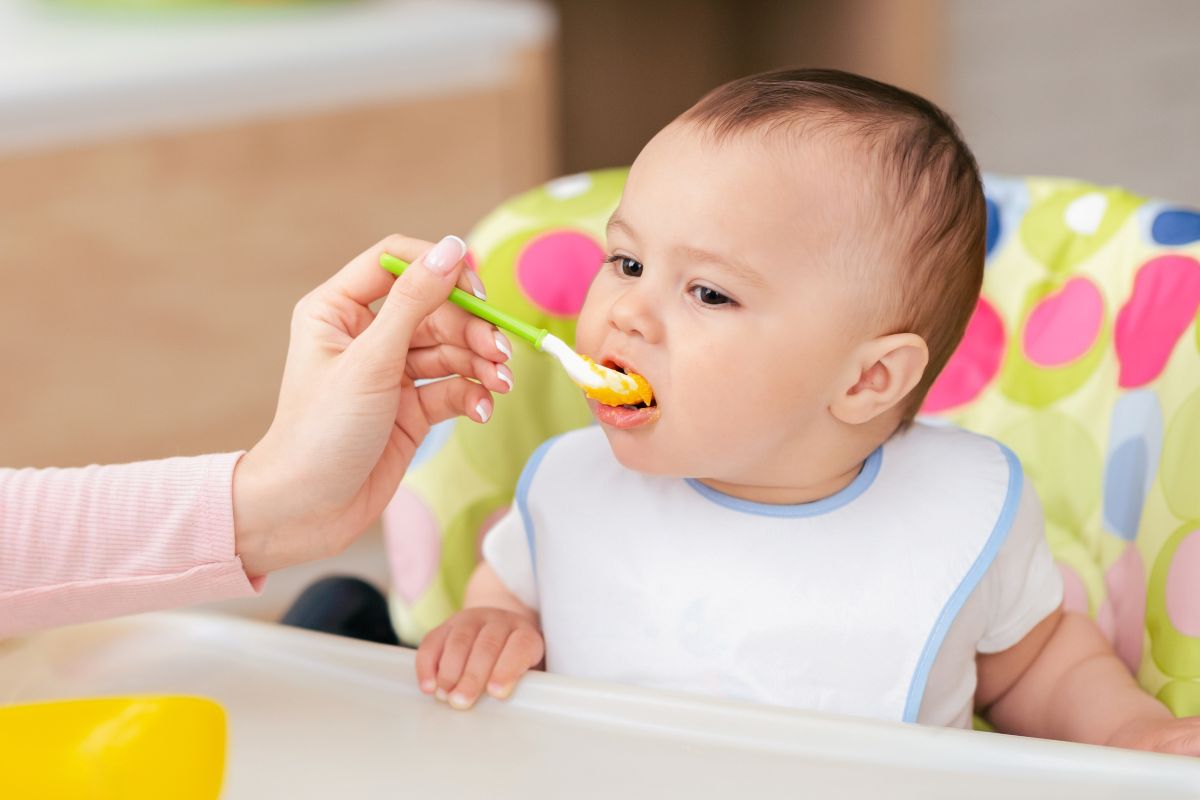 Bambino durante lo svezzamento che assaggia i primi cibi solidi dal cucchiaino.