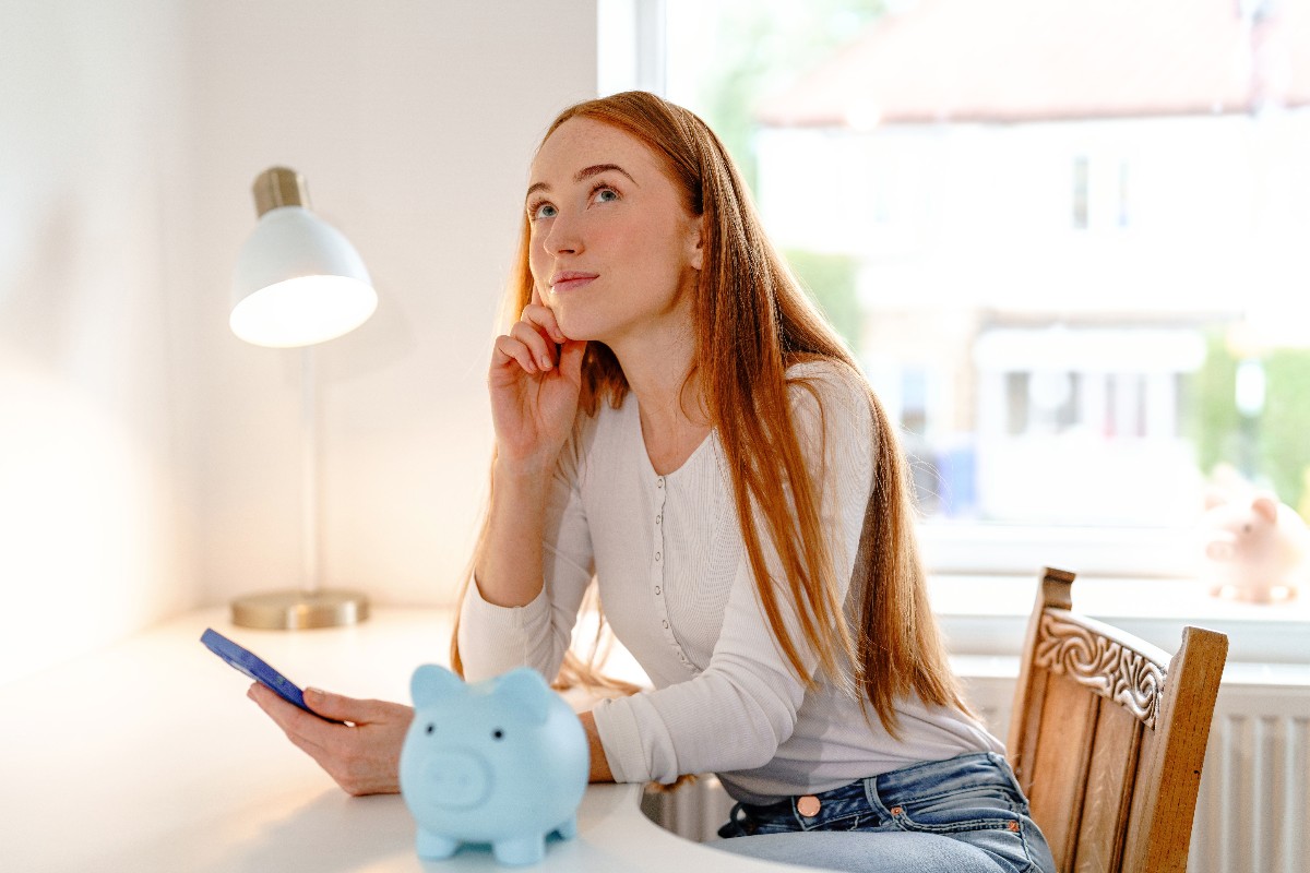 Una ragazza dall'espressione pensierosa con davanti un salvadanaio.