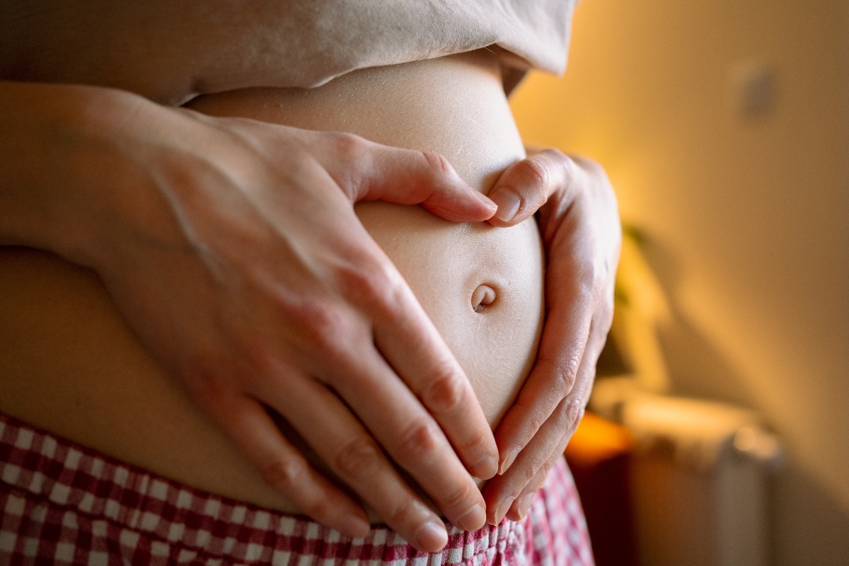 Donna incinta con le mani a forma di cuore sul pancione.